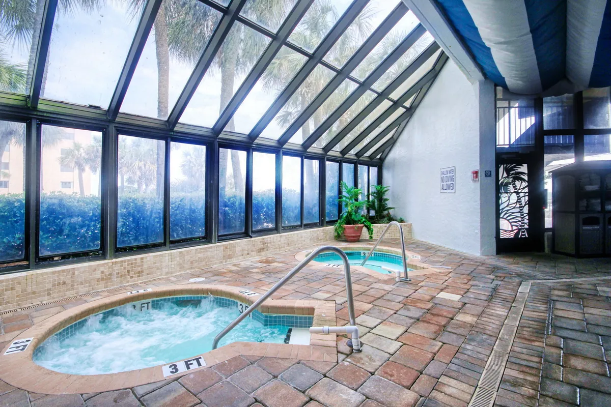 A tranquil interior setting with hot tubs framed by large glass windows and lush potted plants, creating a luxurious space bathed in natural light. The inviting hot tubs offer a perfect retreat for couples to unwind and rejuvenate after a day of adventure.