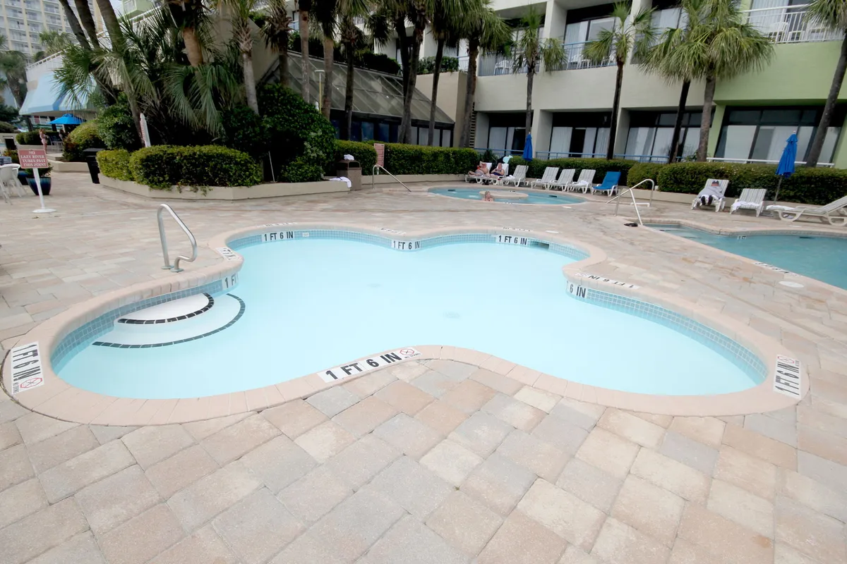 An inviting exterior pool area with a bubbling hot tub, surrounded by palm trees and ample space for lounging or gathering. The scene captures the essence of evening relaxation or vibrant group gatherings under the stars.