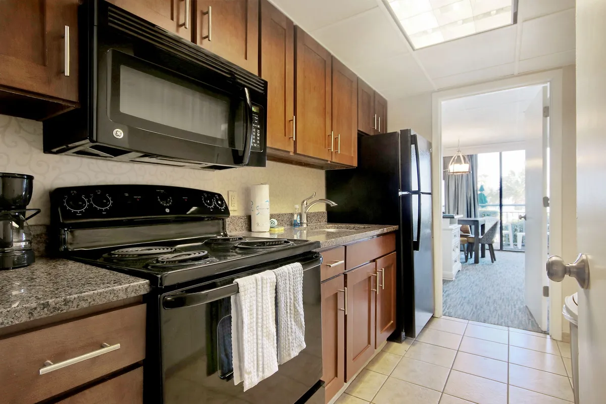 A cozy, functional kitchen features a stove, microwave, kitchen cabinets, and countertop, with a clear doorway providing a view into the adjacent dining area. The space is designed for convenient meal preparation and socializing, with warm lighting and organized surfaces.