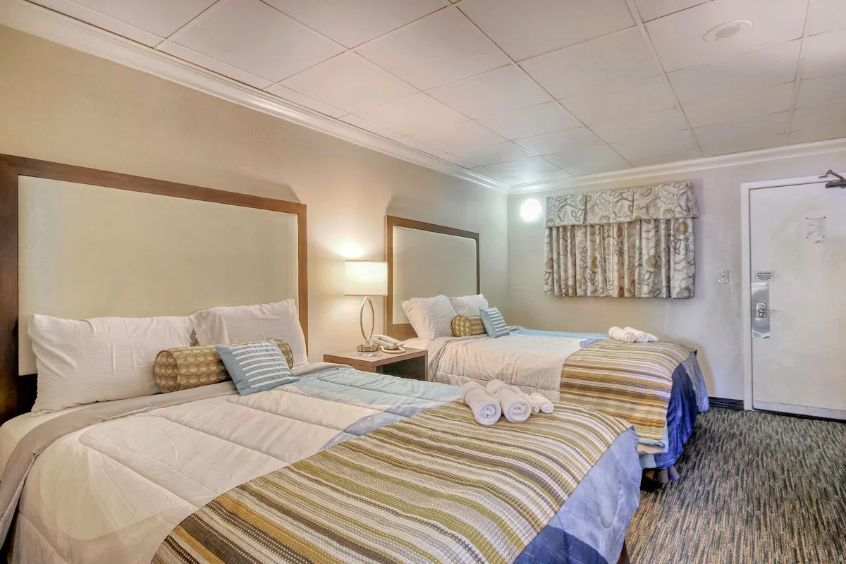 This inviting bedroom features two neatly made beds with soft linens and decorative pillows, a nightstand with a warm lamp, and curtains drawn to create a tranquil retreat. Gentle lighting and thoughtful touches establish an atmosphere ideal for restful nights and peaceful mornings.