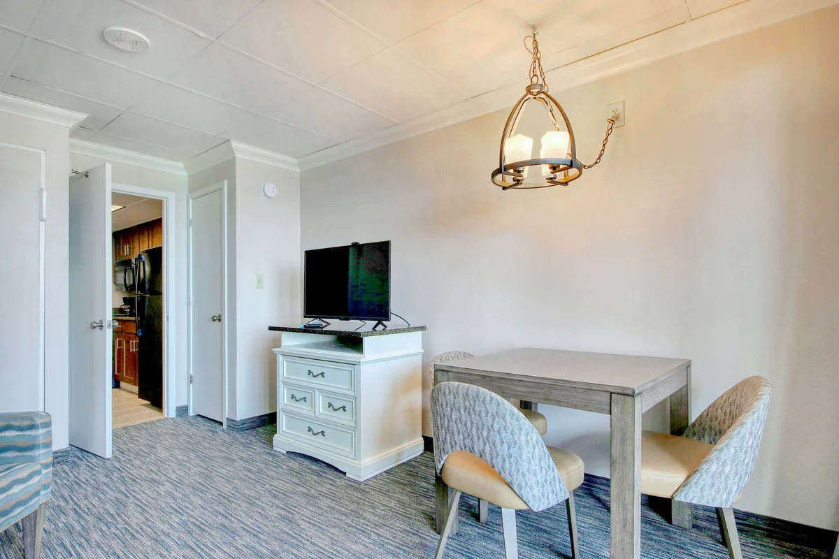 A welcoming dining area is centered around a dining table with chairs, complemented by a chandelier overhead and a television nearby. The setup encourages group meals, casual dining, and shared entertainment, creating a lively atmosphere for togetherness.
