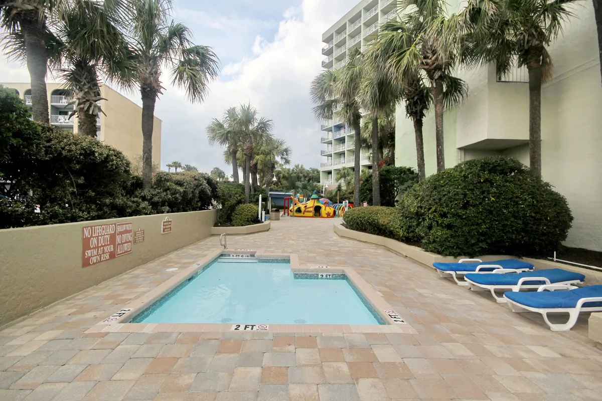 An inviting scene showing a small pool surrounded by lounge chairs, palm trees, and a children’s play area. Families are seen playing together, kids splash in the pool, and the setting feels relaxed and casual—ideal for family bonding and making memories.